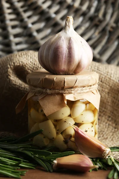 Canned garlic in glass jar and wicker mat and rosemary branches, on wooden background — Stock Photo, Image