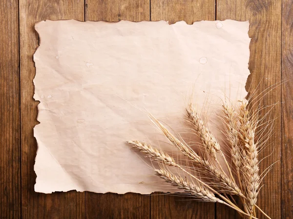 Klásky pšenice s papírem na dřevěné pozadí — Stock fotografie