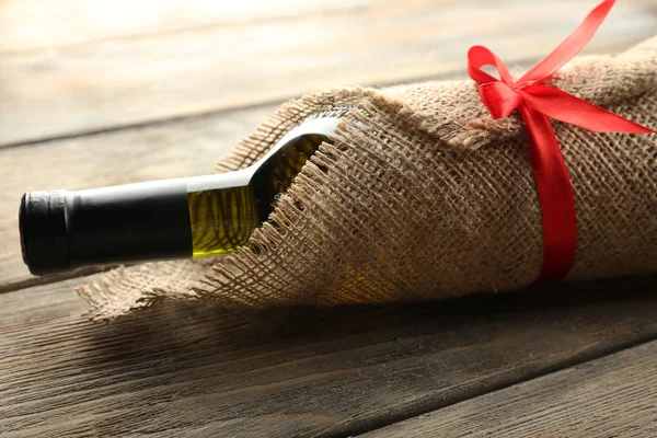 Bottiglia di vino avvolto in panno di iuta su tavole di legno sfondo — Foto Stock