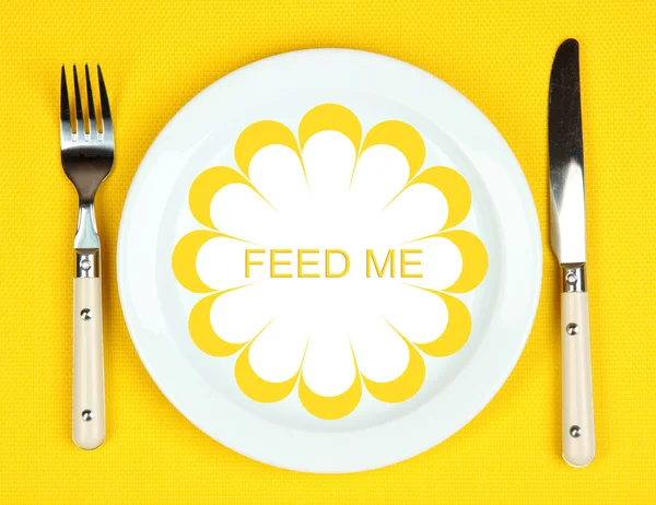 Plate with text Feed Me, fork and knife on tablecloth background — Stock Photo, Image
