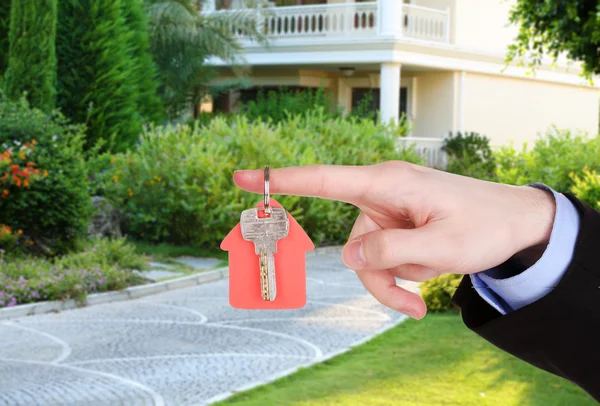 Nyckeln i handen på huset bakgrund, Real estate koncept — Stockfoto