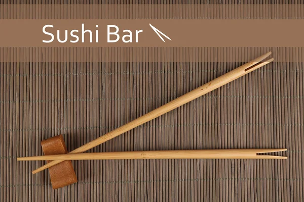 Par de palillos y texto de barra de sushi sobre fondo de estera de bambú marrón —  Fotos de Stock