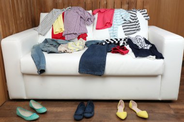 Colorful clothing on white sofa and female shoes on wooden planks background