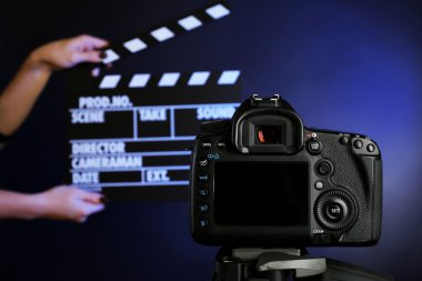 Hands with movie clapper board in front of camera on dark background clipart