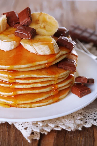 Stapel leckerer Pfannkuchen mit Schokolade, Honig und Bananenscheiben auf Teller und Serviette auf Holztischhintergrund — Stockfoto