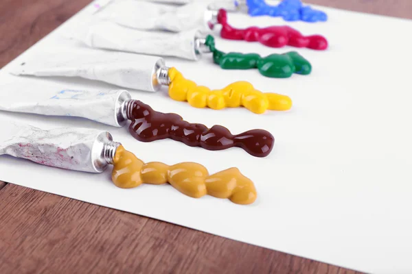 Bunte Farbtuben auf weißem Papier und hölzernem Tischhintergrund gequetscht — Stockfoto