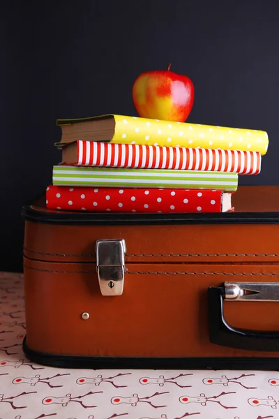 Valise vintage avec pile sur livres sur surface à motifs et fond sombre — Photo