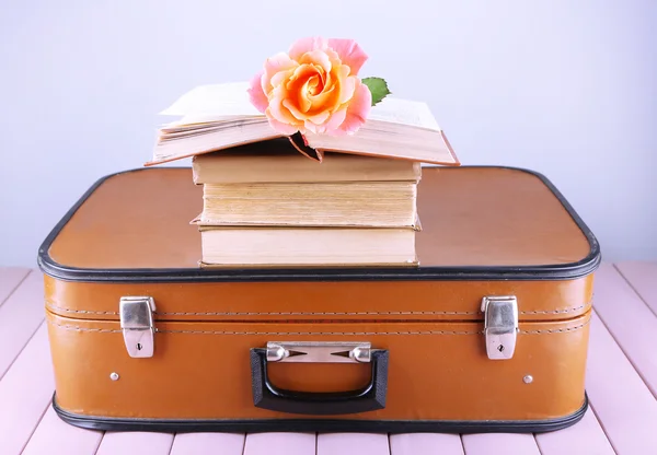 Vintage suitcase with pile on books on patterned surface and light background — Stock Photo, Image