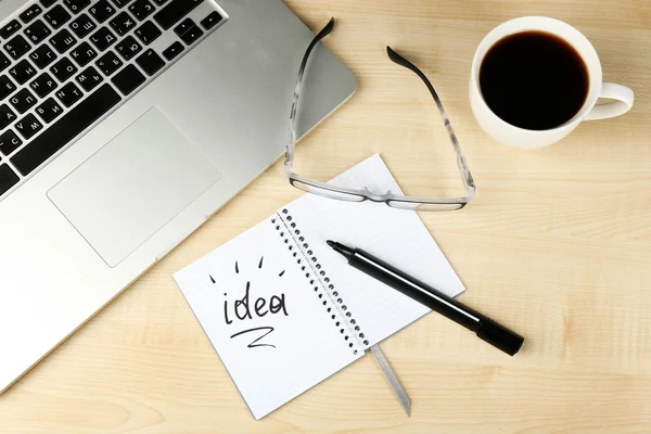 Cup of coffee with note Idea in notebook and glasses on wooden table background — Stock Photo, Image