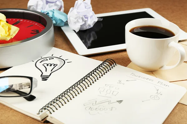 Symbole de l'idée comme ampoule dans un carnet avec papier froissé, tablette et tasse de café sur fond de bureau en bois — Photo