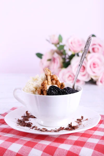 Десерт с черносливом в чашке с букетом роз на цветном деревянном столе и светлом фоне — стоковое фото
