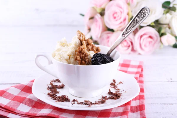 Dessert with prunes in cup with bouquet of roses on color wooden table background — Stock Photo, Image