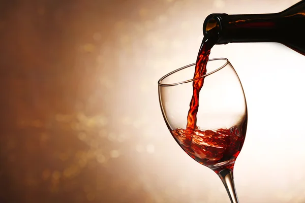 Giet rode wijn uit fles in glas op kleur achtergrond — Stockfoto
