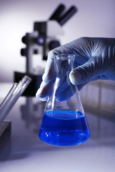 Artículos de vidrio de laboratorio con líquido azul en la mano del científico sobre fondo gris —  Fotos de Stock