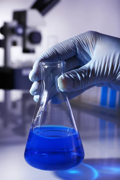 Artículos de vidrio de laboratorio con líquido azul en la mano del científico sobre fondo gris — Foto de Stock