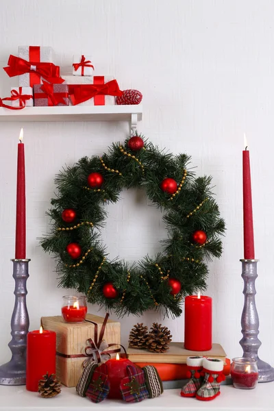 Χριστουγεννιάτικη διακόσμηση με στεφάνι, κεριά και παρόντες κουτιά στο ράφι σε φόντο λευκό τοίχο — Φωτογραφία Αρχείου