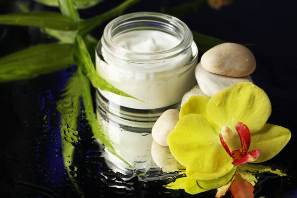 Face cream with orchid flowers on dark background