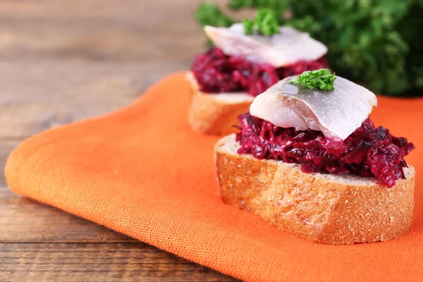 Rye toasts with herring and beets on napkin on wooden table — Stock Photo, Image