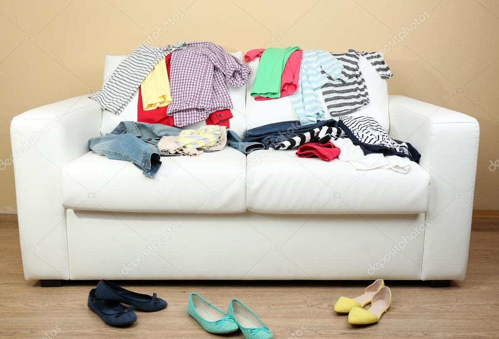 Colorful clothing on white sofa and female shoes on light wall background