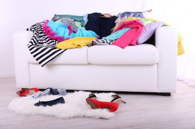 Messy colorful clothing on  sofa on light background clipart