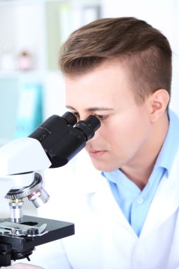 Erkek bilim adamı laboratuvarda mikroskop kullanıyor.