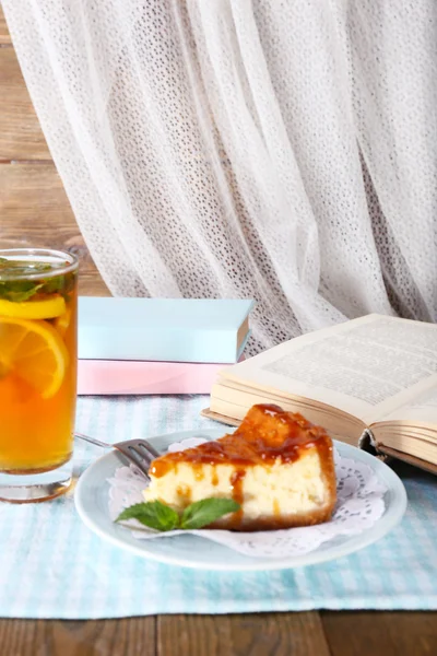 Bolo de queijo em prato, xícara de chá e livros em toalha de mesa no fundo da cortina — Fotografia de Stock