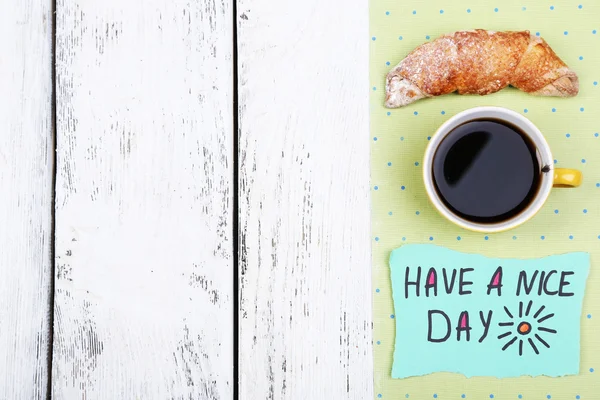 Composición de café, croissant fresco y tarjeta de papel sobre servilleta, sobre fondo de madera —  Fotos de Stock