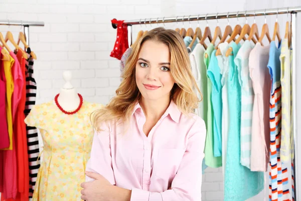 Beautiful young stylist near rack with hangers — Stock Photo, Image