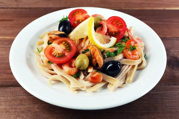 Tasty pasta with shrimps, mussels, black olives and tomato sauce on plate on wooden background — Stock Photo, Image