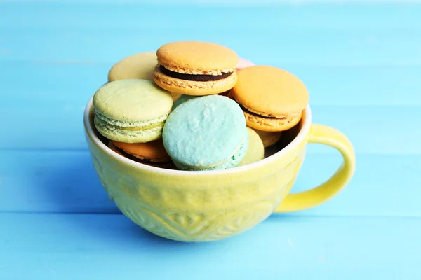 Assortimento di delicati macaron colorati in tazza colorata su sfondo di legno a colori — Foto Stock