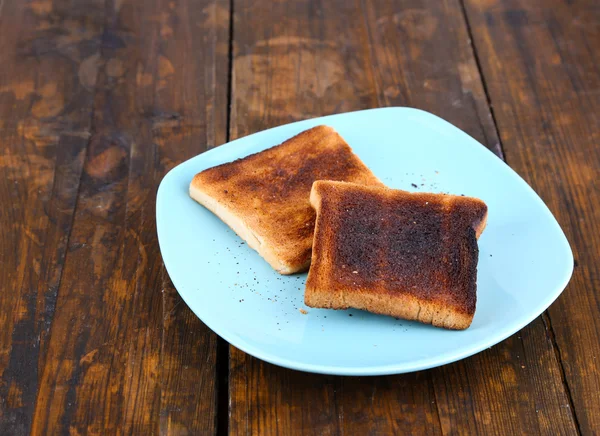 Pane tostato bruciato su piatto turchese, su sfondo tavolo di legno — Foto Stock