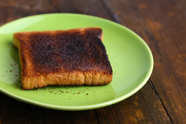 Pane tostato bruciato su piatto verde chiaro, su sfondo tavolo di legno — Foto Stock