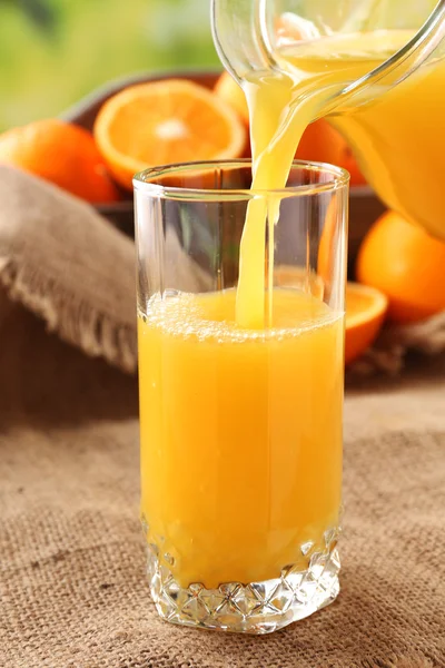 Pouring orange juice from glass carafe, on wooden table and bright background — Stock Photo, Image