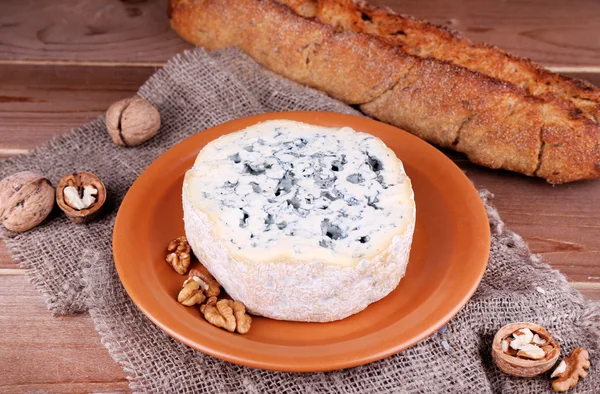 Blue cheese on earthenware dish with nuts and baguette on burlap cloth and wooden table background — Stock Photo, Image