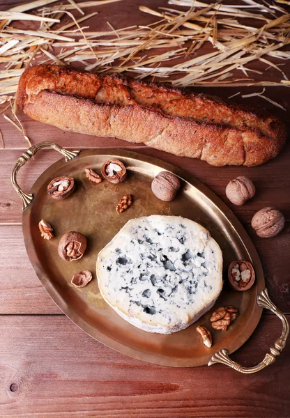 Blue cheese with nuts, baguette and hay on metal tray and wooden table background — Stock Photo, Image