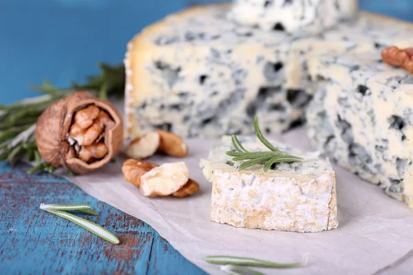 Queijo azul com raminhos de alecrim e nozes em folha de papel e cor de fundo de mesa de madeira — Fotografia de Stock