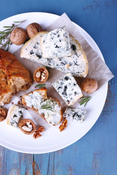 Queso azul con ramitas de romero, pan y nueces en plato y fondo de mesa de madera de color — Foto de Stock