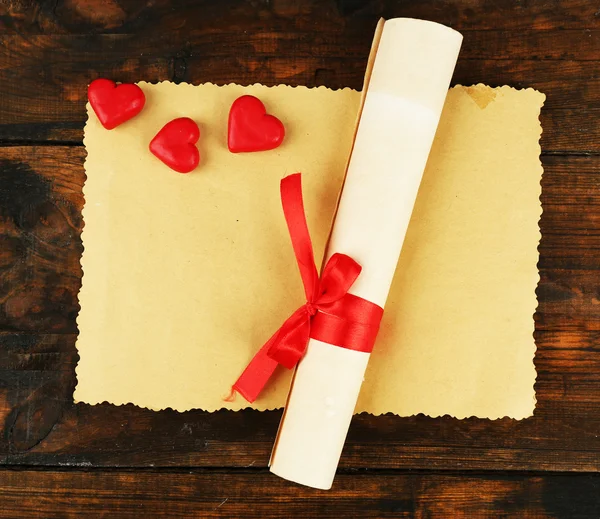 Roll and sheet of paper with hearts on rustic wooden table background — Stock Photo, Image