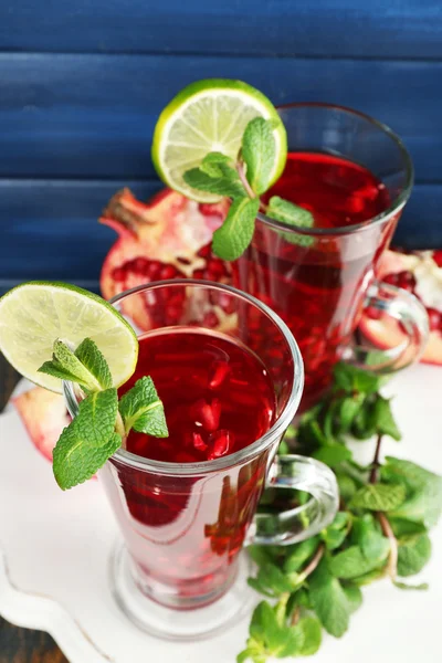 Granatäpple dryck i glas med mynta och skivor av kalk på plattan och färg trä bakgrund — Stockfoto