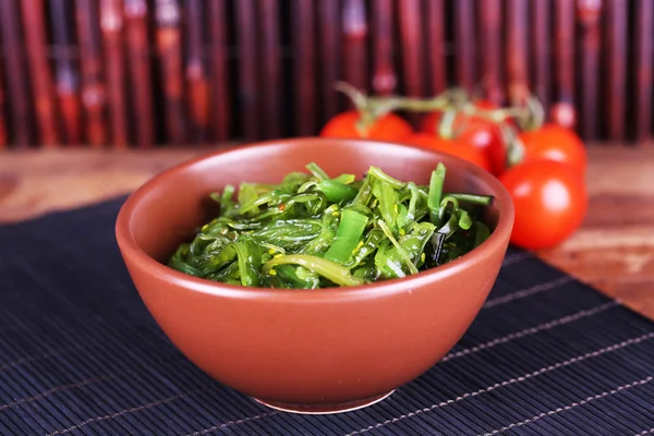 Salade d'algues dans un bol avec tomates cerises sur fond de tapis de bambou — Photo