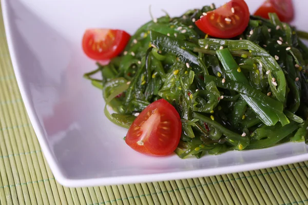 Ensalada de algas con rodajas de tomate cherry sobre fondo de bambú — Foto de Stock