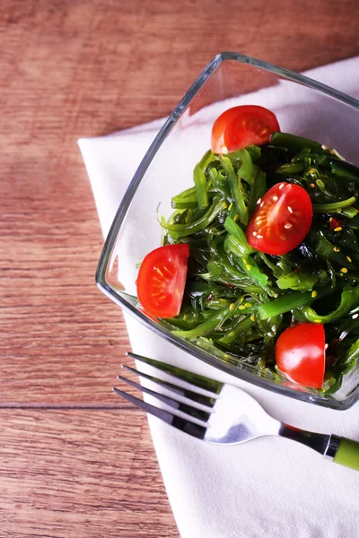 Ensalada de algas marinas con rodajas de tomate cherry en un tazón de vidrio sobre servilleta y fondo de mesa de madera —  Fotos de Stock