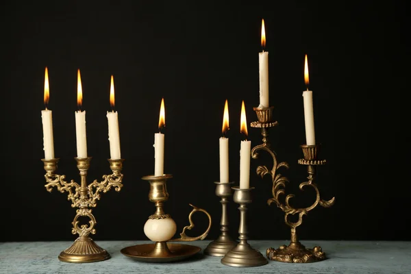 Retro candlesticks with candles on wooden table, on black background — Stock Photo, Image