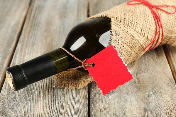 Wine bottle wrapped in burlap cloth on wooden planks background