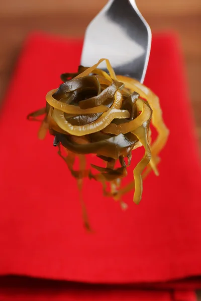 Algas sobre tenedor con servilleta roja y fondo de mesa de madera — Foto de Stock