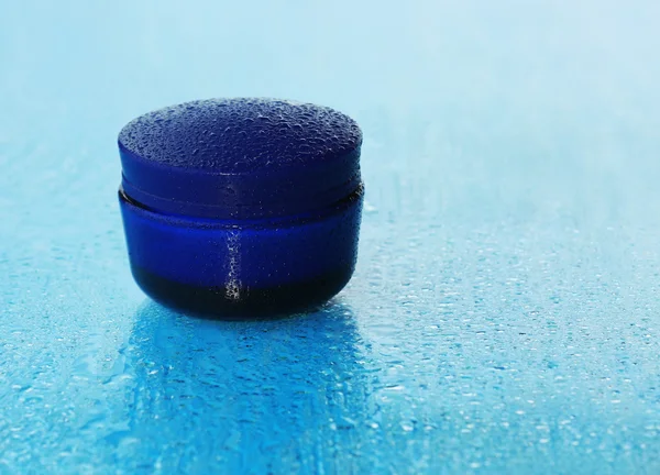 Kosmetikcreme auf blauem Hintergrund mit Wassertropfen — Stockfoto