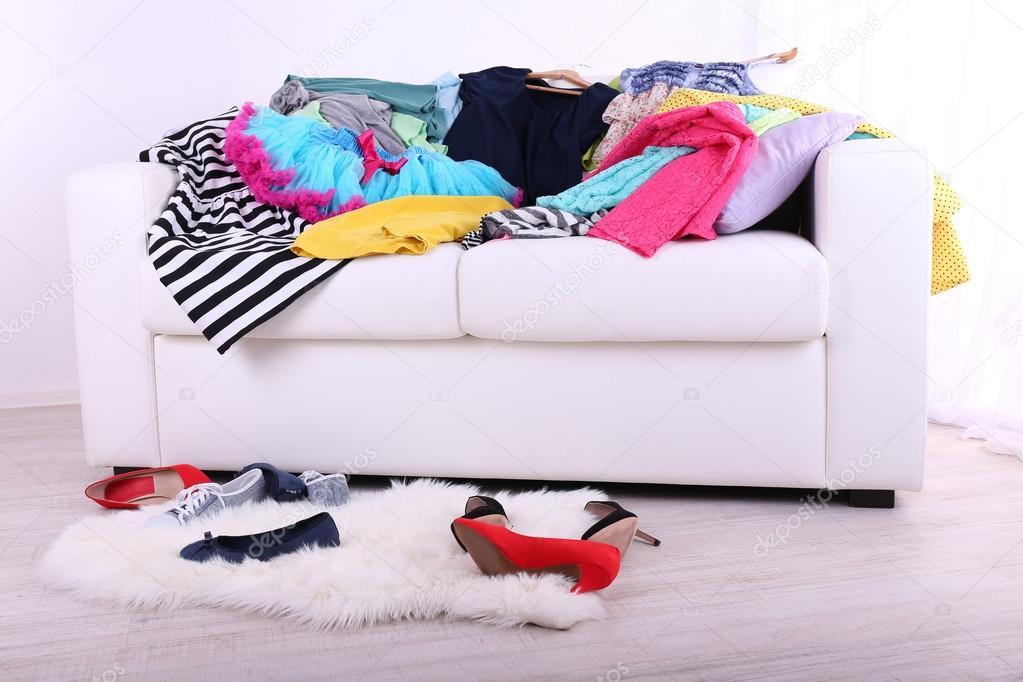 Messy colorful clothing on  sofa on light background