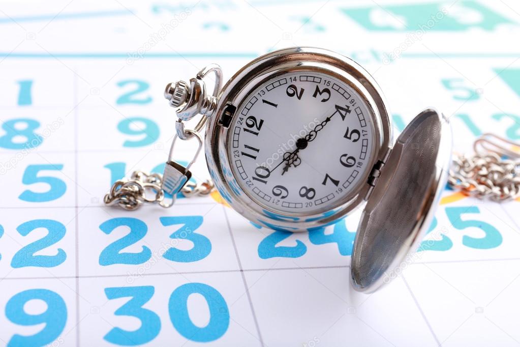 Silver pocket clock on calendar background