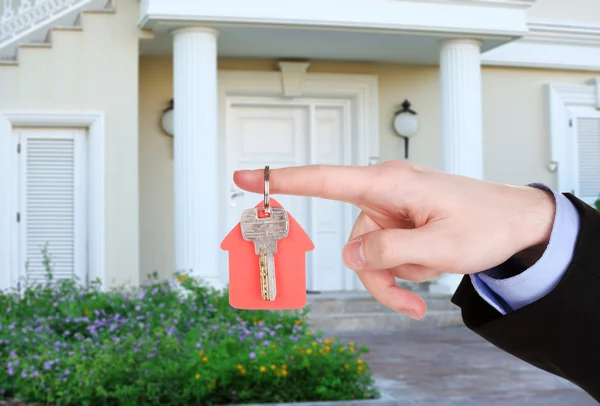 Llave en mano en el fondo de la casa, concepto de bienes raíces —  Fotos de Stock