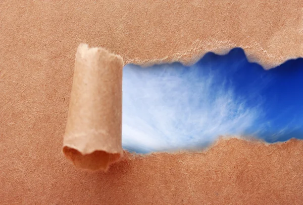 Sfondo cielo blu con nuvole attraverso strappato carta artigianale — Foto Stock